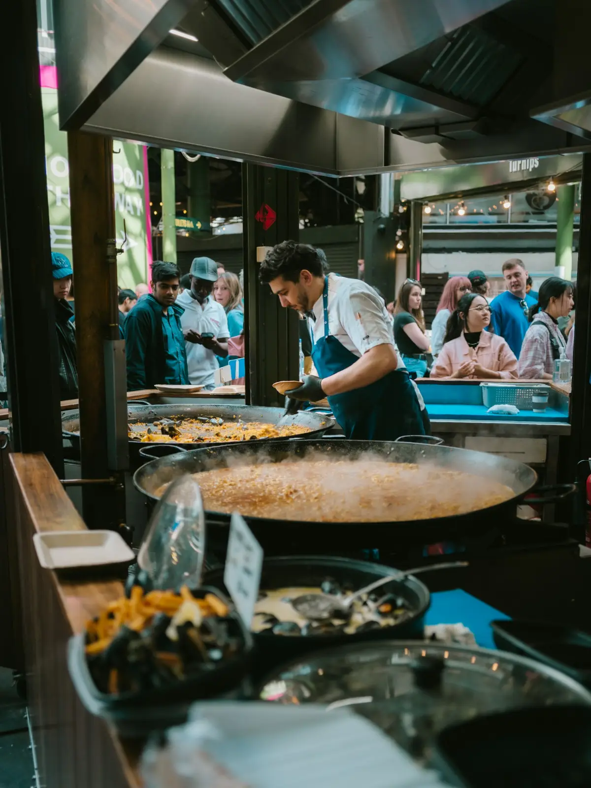 A chef cooking paella in a large pan at a busy market stall
