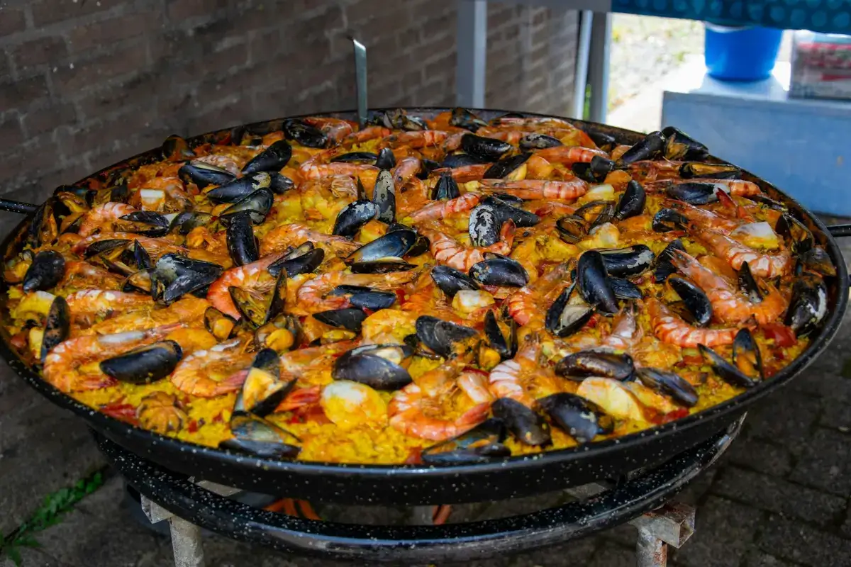 A giant pan of seafood paella with mussels and prawns cooking over a burner