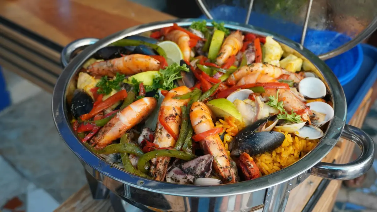 Paella topped with whole prawns, clams and peppers in a steel pan