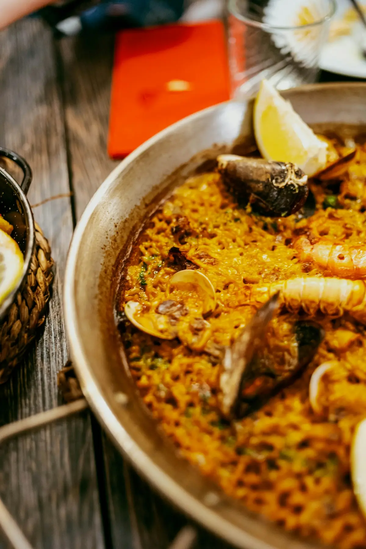 Paella with lemon wedges in a pan on a rustic wooden table