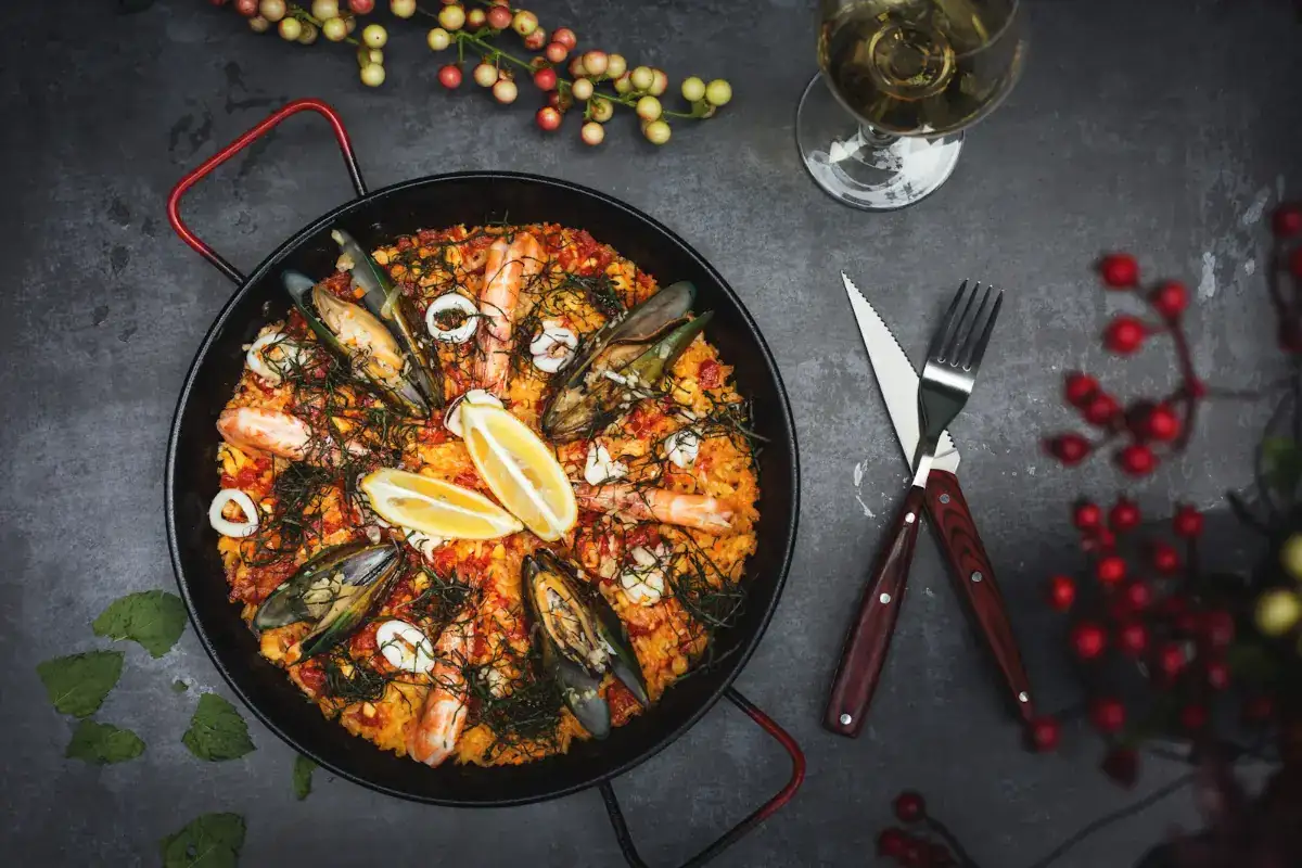 Seafood paella in a black pan with lemon wedges on a dark table