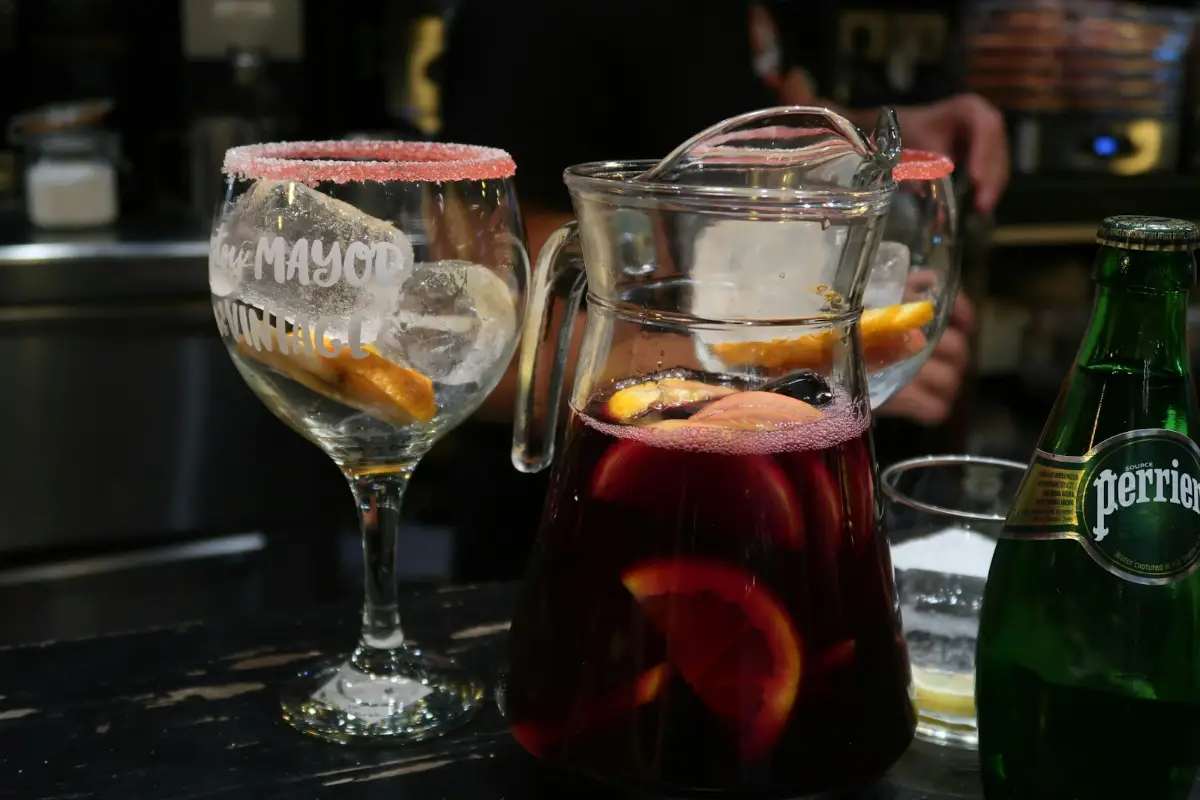 A jug of red sangria with orange slices next to a glass