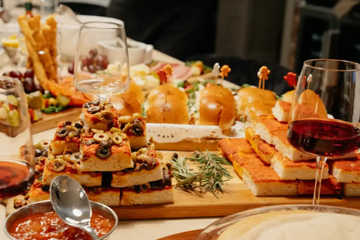 A spread of tapas on wooden boards with glasses of red wine
